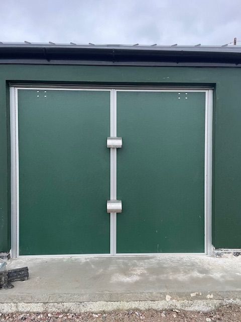 A brick building with green doors and a roof