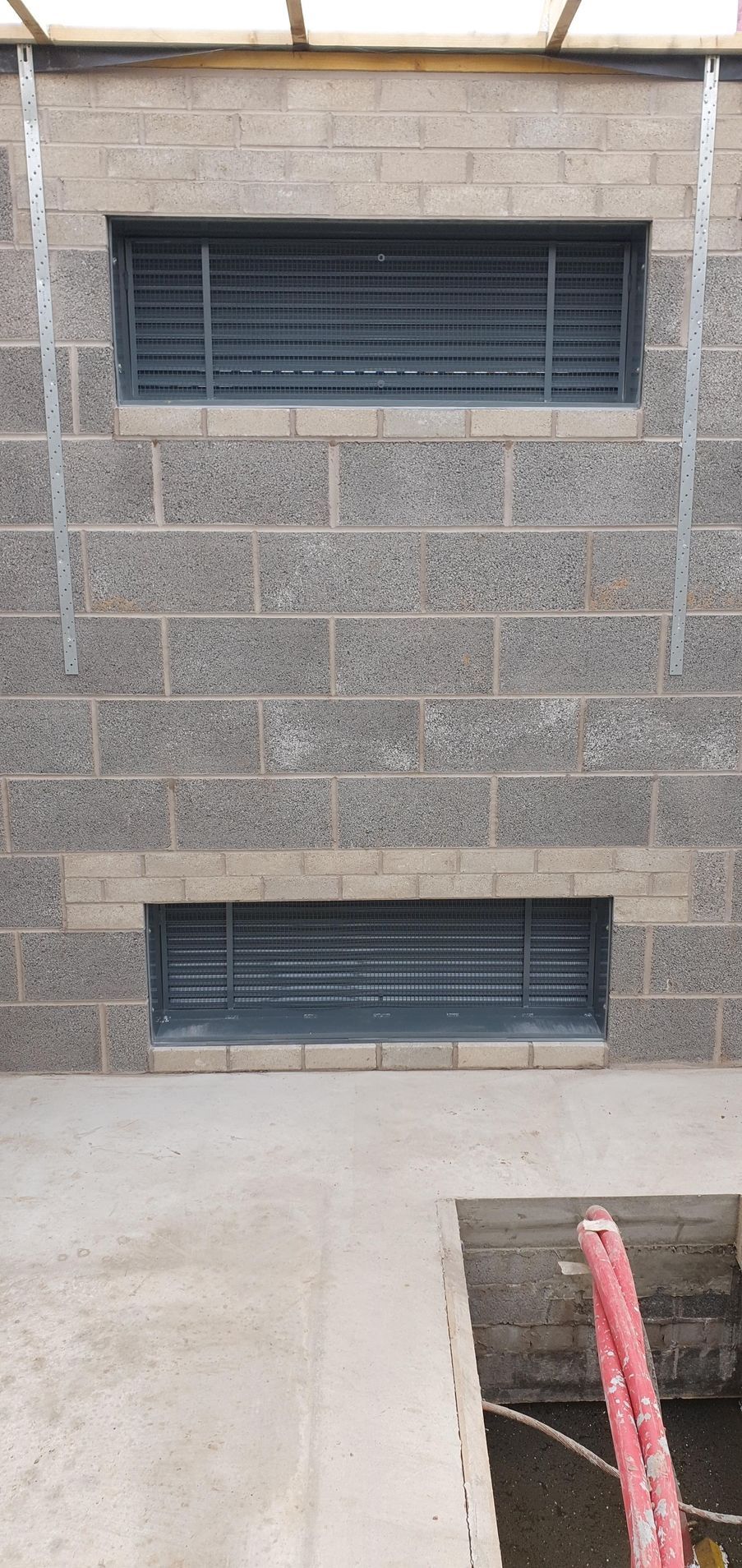 A brick wall with two windows and a hole in the ground.
