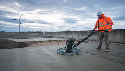 A worker power trowels Ready Mix Concrete in Addis Ababa to create a smooth finish on a large outdoor concrete slab.