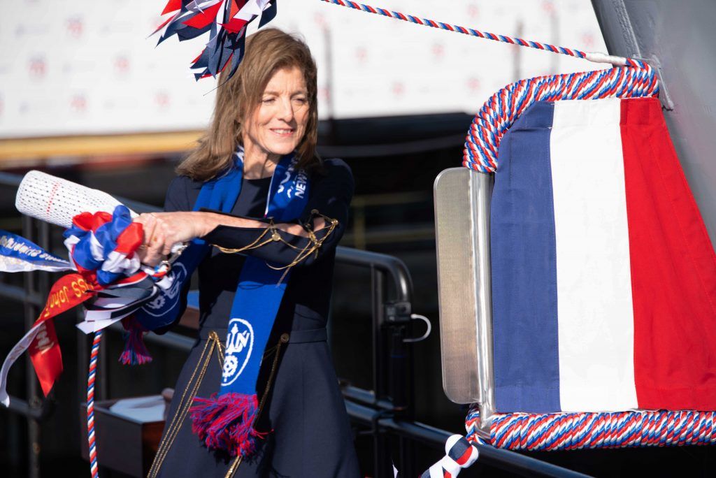 A woman is standing next to a red , white and blue flag.