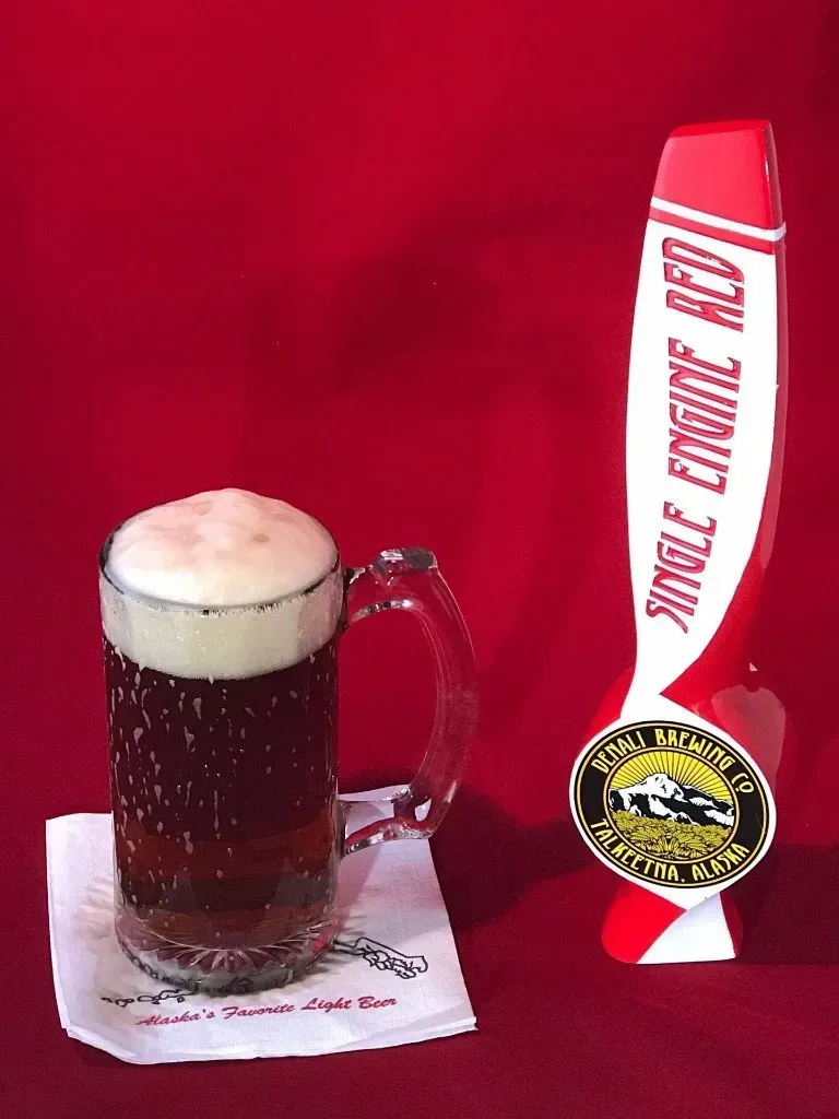 A glass of beer next to a single engine red beer tap