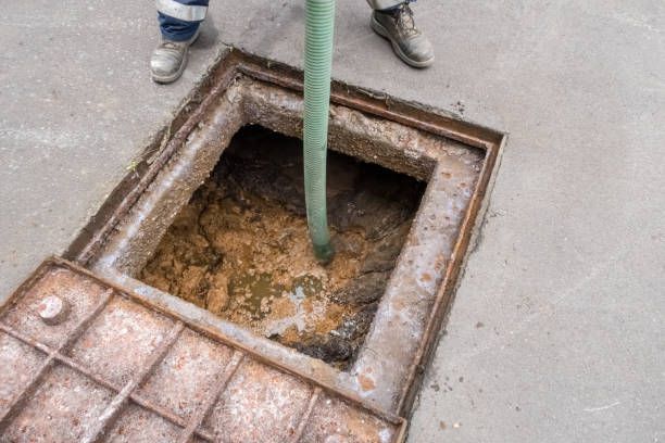 Worker with hose pumping waste from open manhole.