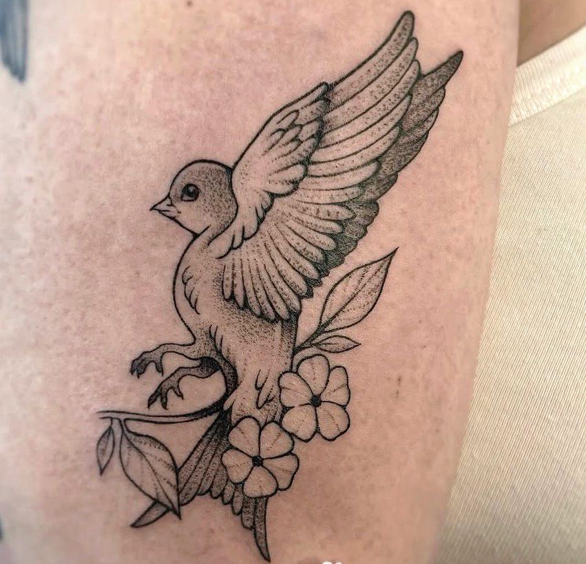 Black and gray tattoo by Jacy Andrew depicting a small bird with raised wings perched among flowers and leafy branches, featuring fine lines and dotwork shading.