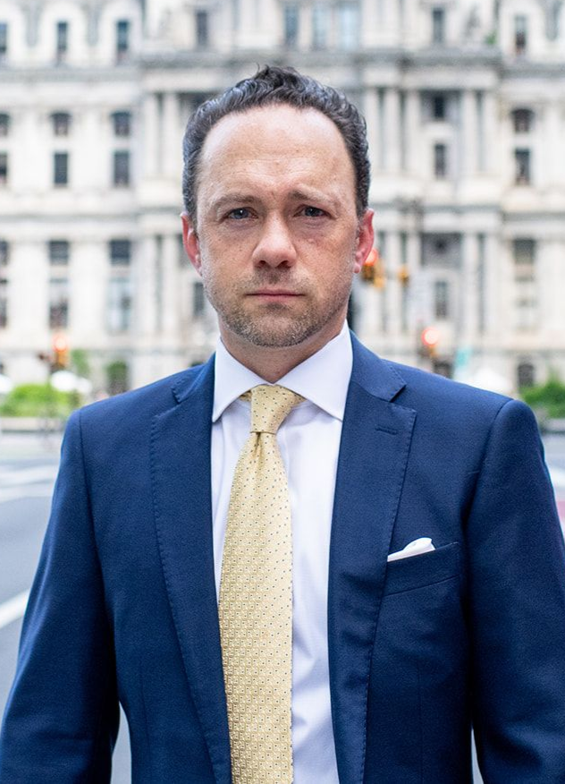 Man in a blue suit and yellow tie standing outdoors before a building.