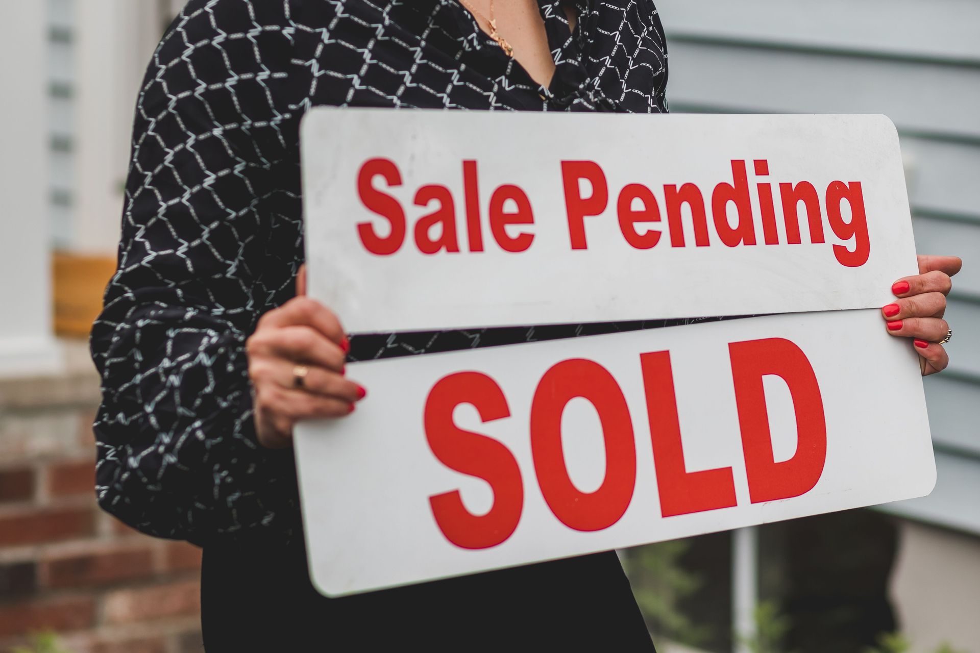Person holding a real estate sign reading “Sale Pending” and “SOLD”