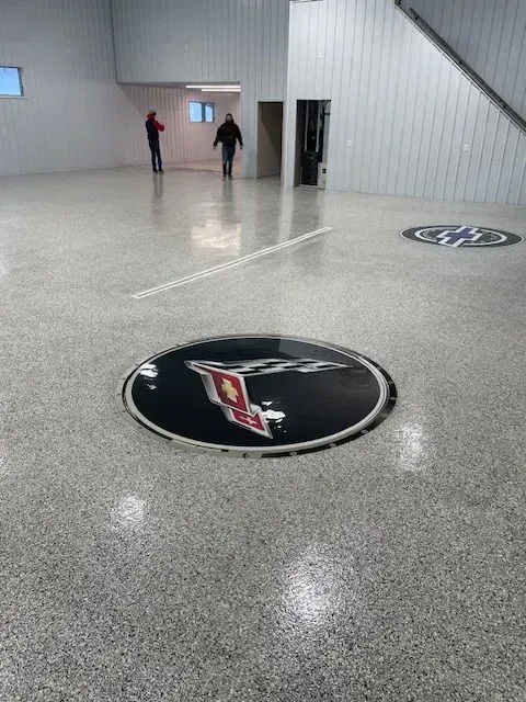 Epoxy floor with car logos. Two people walking in a garage with white walls and stairs.