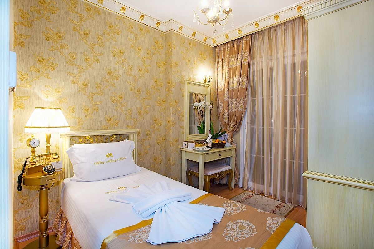 White house hotel,Cozy bedroom with a single bed, warm yellow decor, lamp, vanity, and sheer curtains