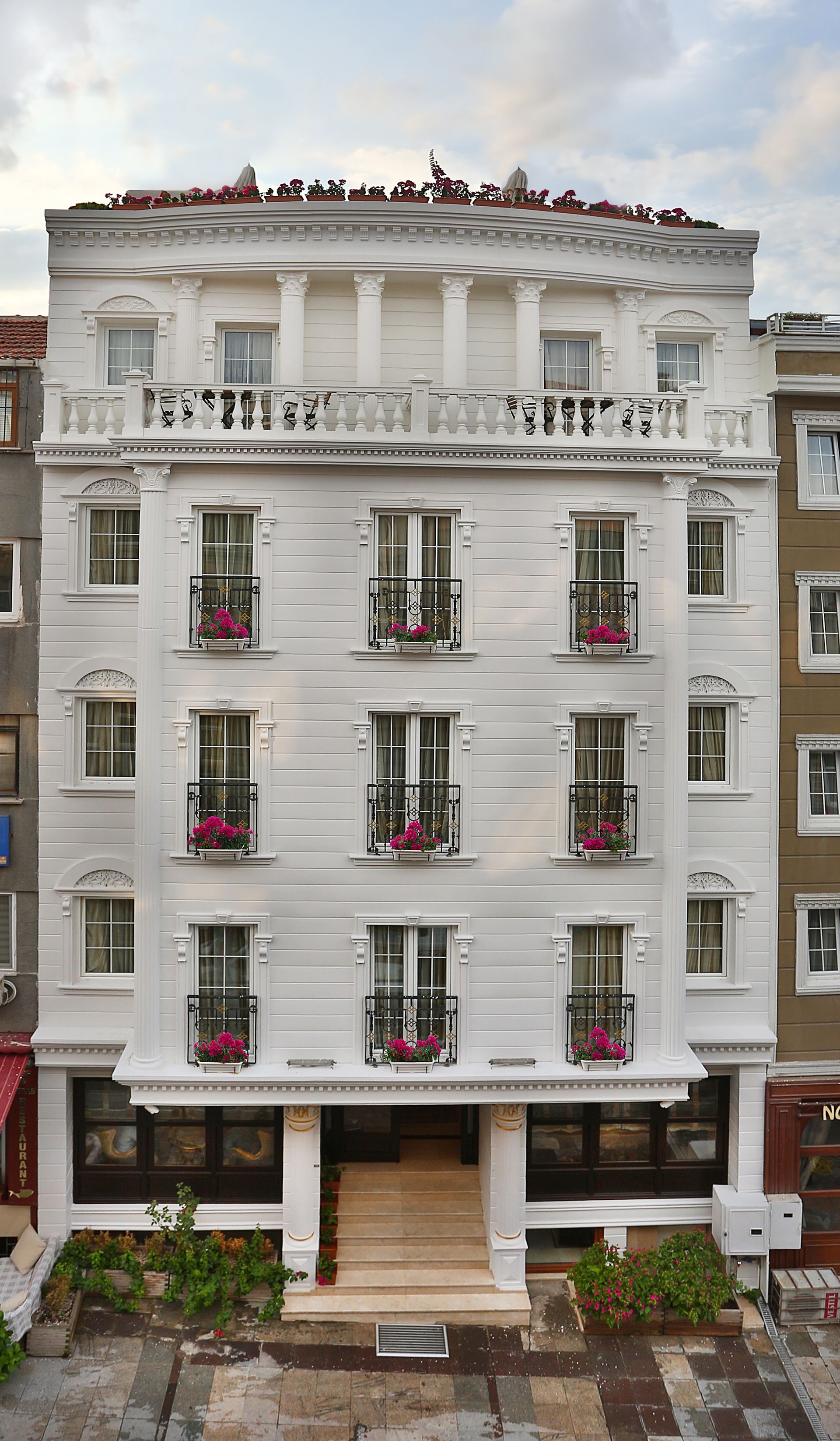 Istanbul white house hotel | White multi-story hotel with balconies and pink flowers in front of a cloudy sky
