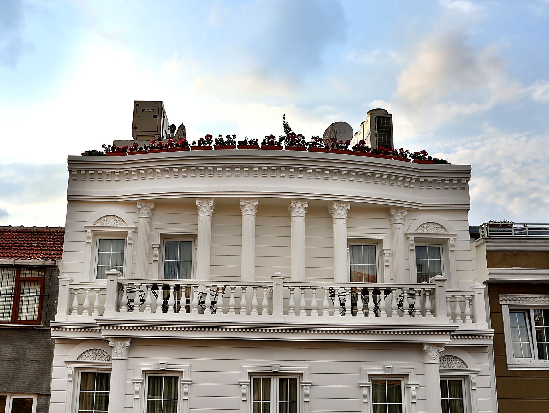 White ornate hotel building with rooftop people and plants under a cloudy sky