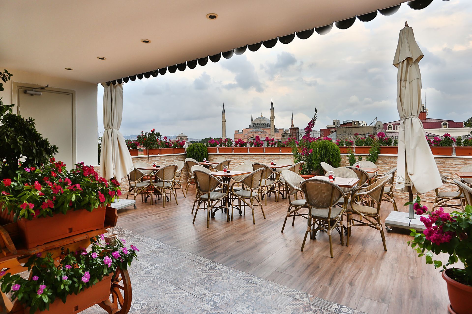 Istanbul white house hotel | Outdoor café terrace with wicker tables, pink flowers, and city skyline views under a cloudy sky