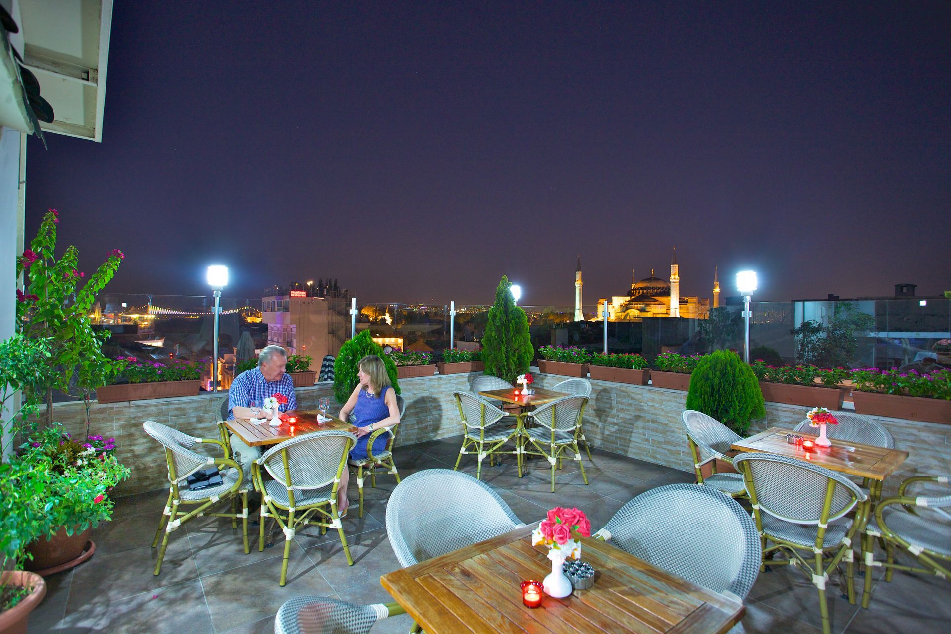 Rooftop patio with people dining at tables overlooking a city skyline at night
