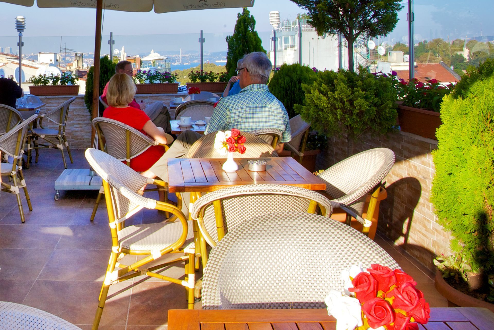 Istanbul white house hotel | Outdoor café patio with wicker chairs, tables, and two seated people at sunset.