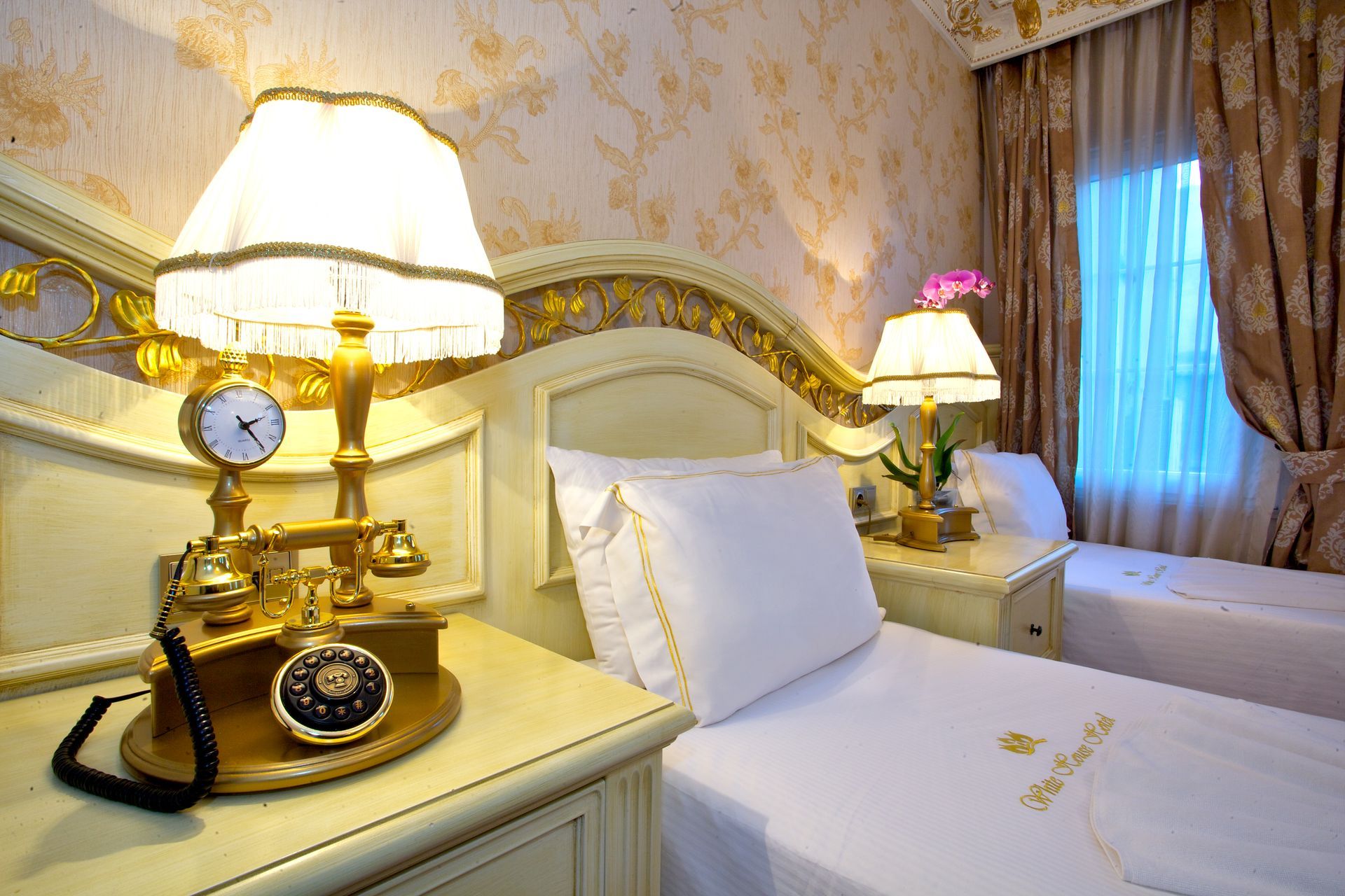Istanbul white house hotel | Elegant hotel room with two neatly made beds, gold lamps, and ornate decor by a curtained window