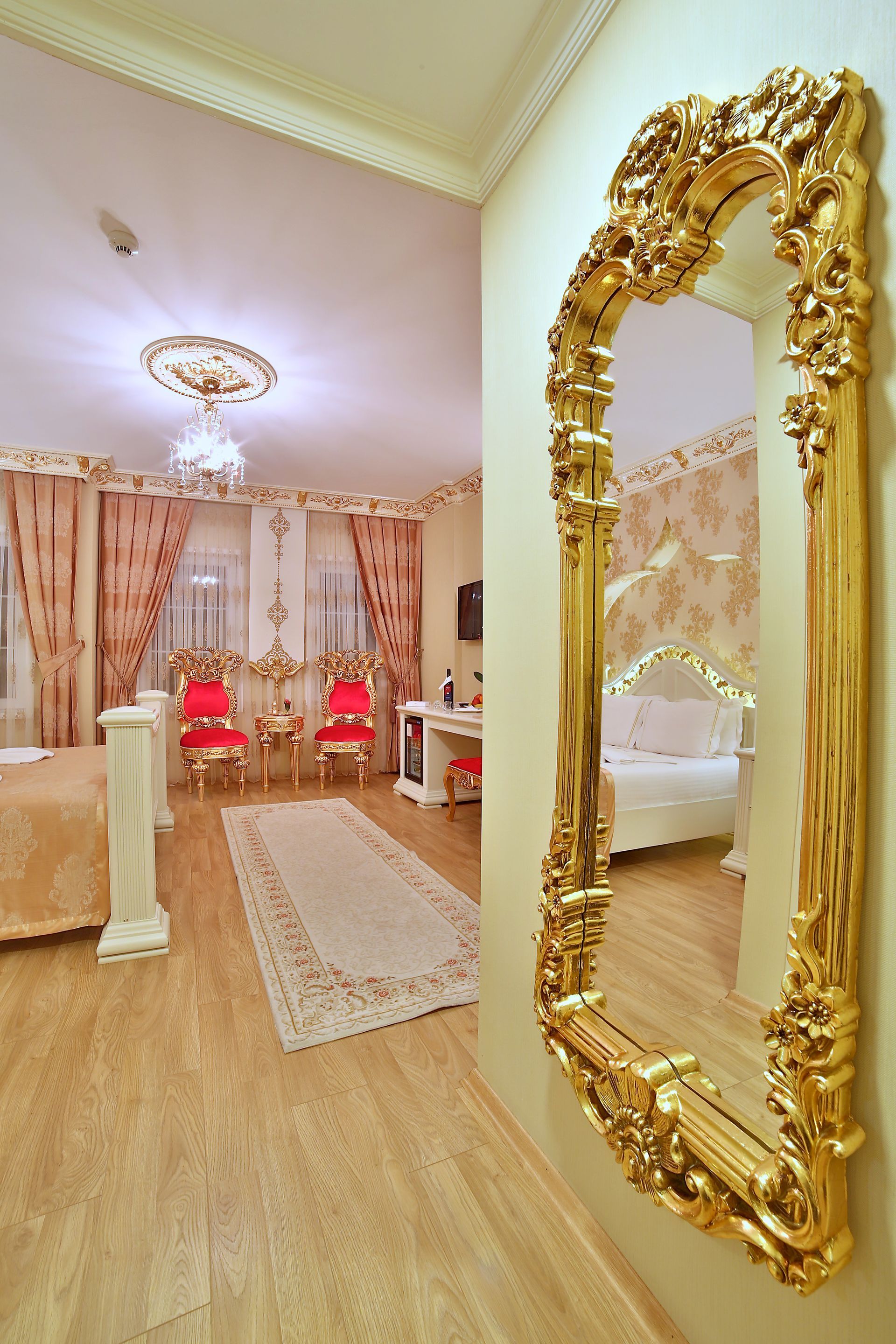 Istanbul white house hotel | Elegant living room with gold mirror, pink chairs, chandelier, and curtains.