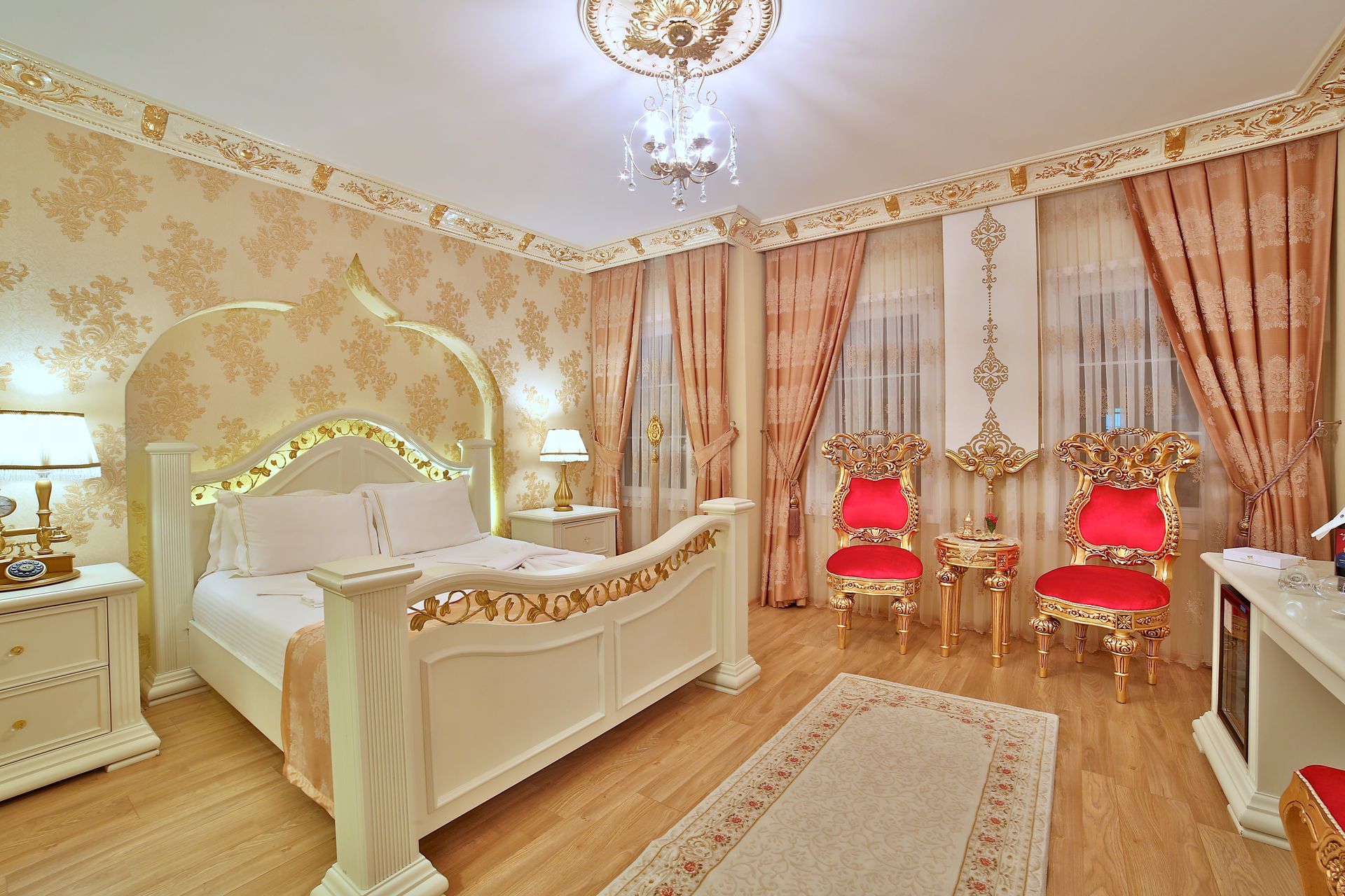 Istanbul white house hotel | Elegant cream bedroom with ornate white bed, chandelier, and two red chairs by draped windows