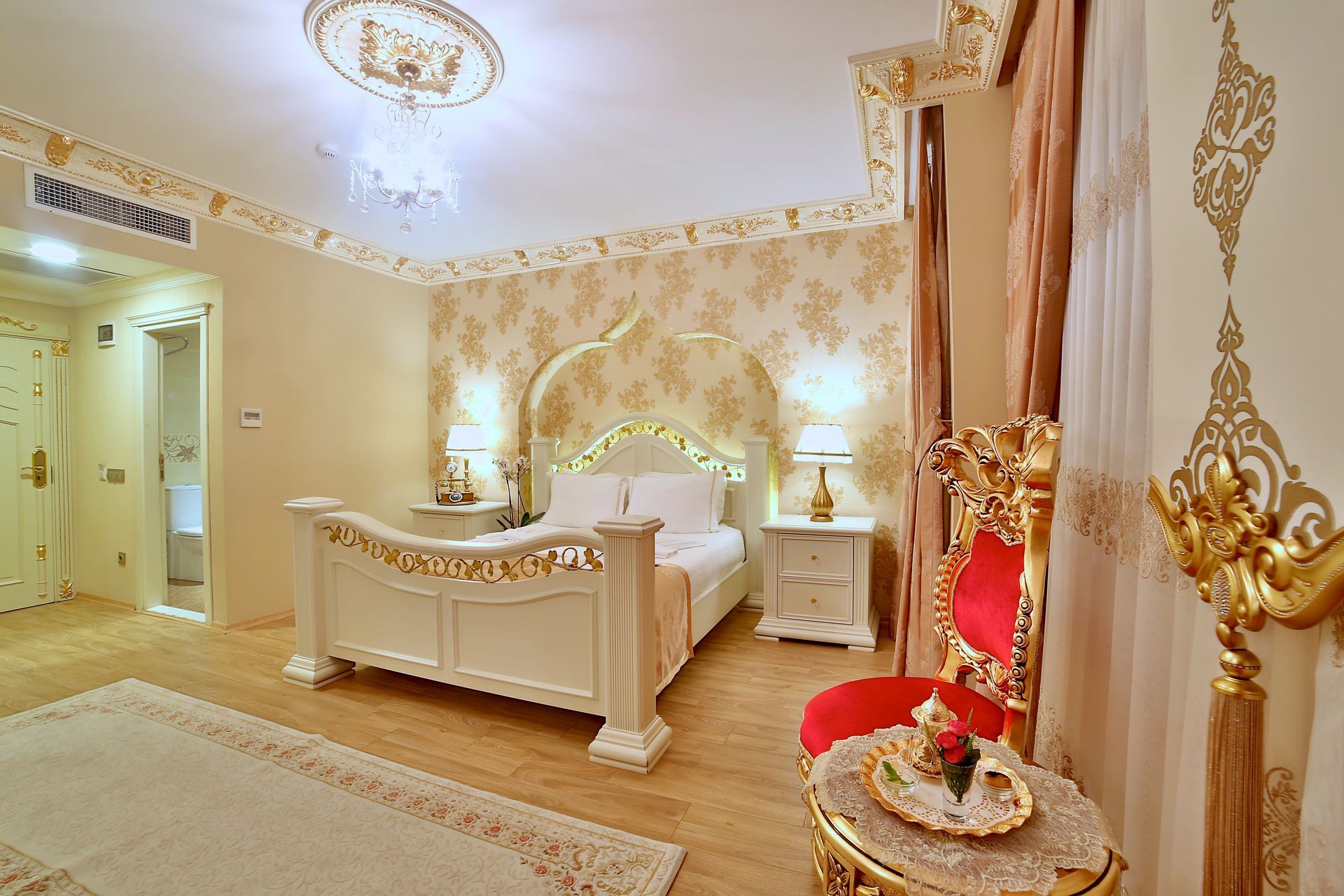Istanbul white house hotel | Elegant cream-and-gold bedroom with ornate bed, chandelier, curtains, and red accent chair