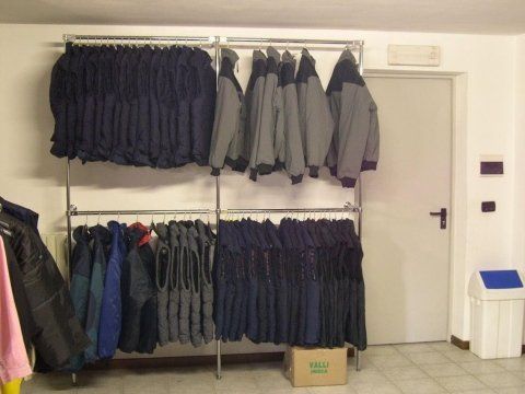 Cappotti e pantaloni appesi su attaccapanni metallici in un corridoio vicino a una porta.