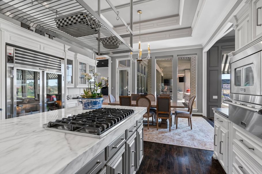 Bright white luxury kitchen with marble island, gas stove, and open dining area with large windows