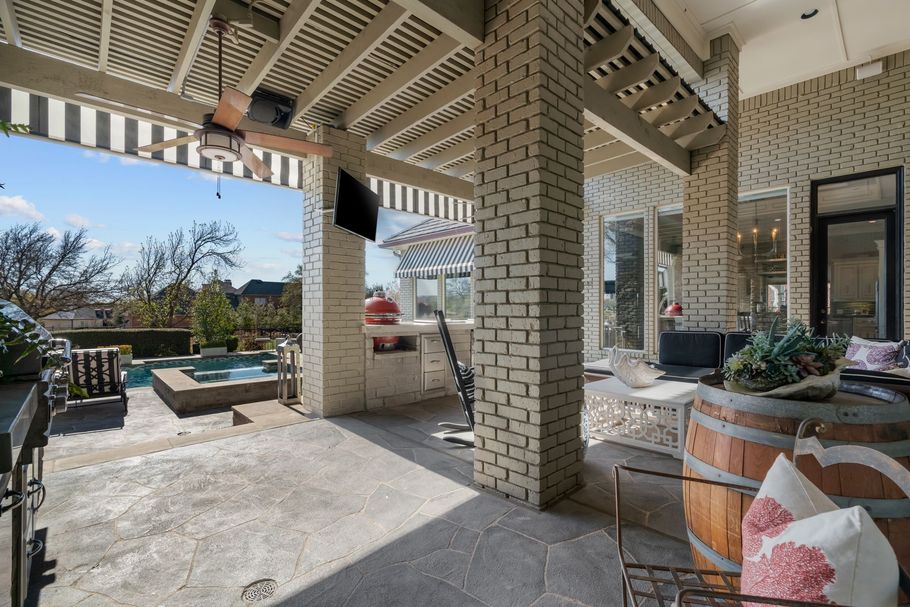 Covered patio with brick columns, lounge seating, and outdoor dining area overlooking a backyard pool