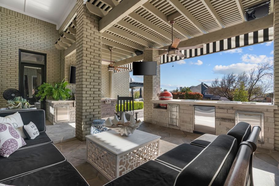 Covered patio with black wicker seating, white coffee table, brick columns, and striped awning overlooking a yard.