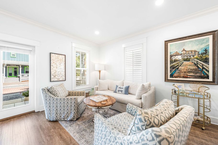 Bright living room with patterned armchairs, sofa, lamp, wall art, and a large window.