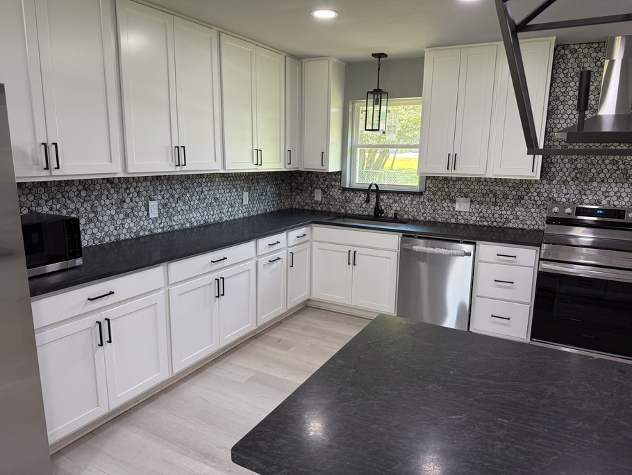 Bright modern kitchen with white cabinets, black countertops, and mosaic tile backsplash.