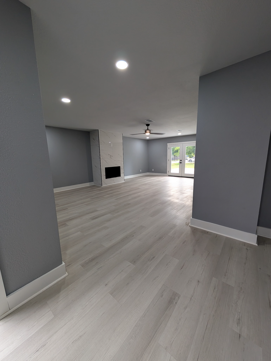 Empty gray open-plan room with light wood floors, recessed lights, ceiling fan, and sliding glass doors.