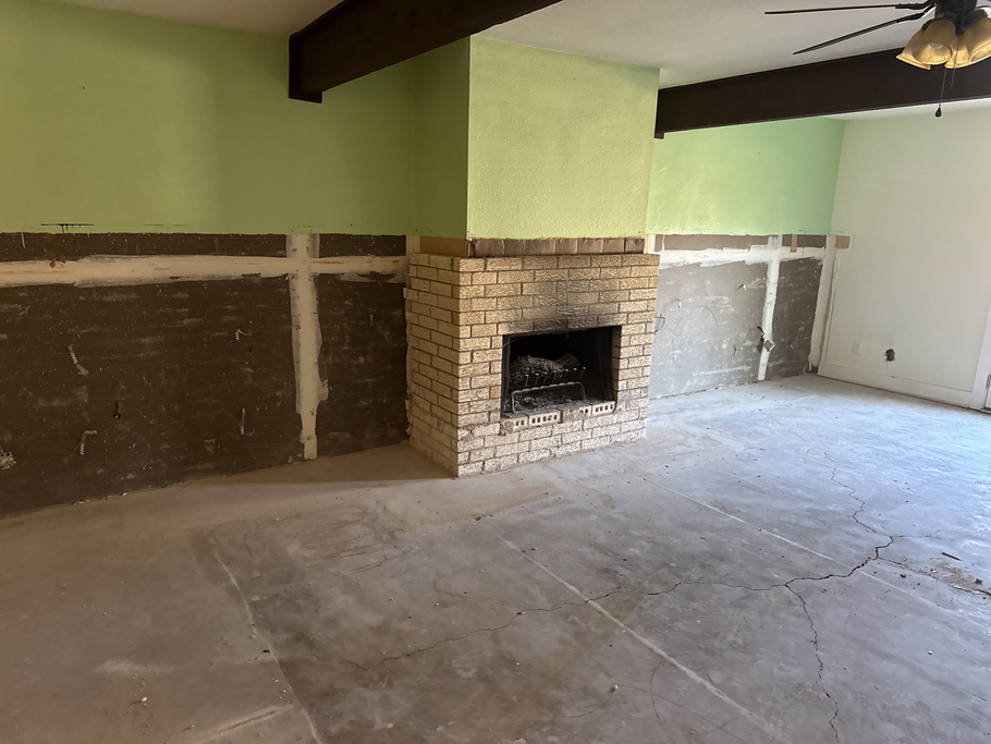 Empty living room with a stone fireplace, green and white walls, and unfinished concrete floor
