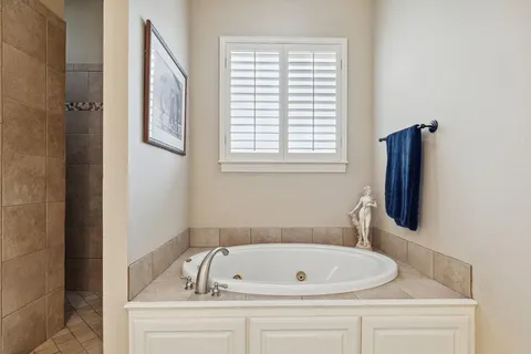 Bathroom with a white soaking tub, tiled shower, shuttered window, and blue towel