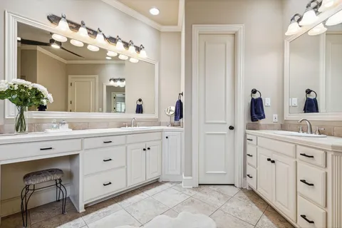 Bright bathroom with double vanity, large mirror, white cabinets, and tiled floor