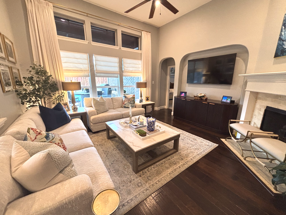 Bright living room with beige sofas, coffee table, fireplace, TV, and large windows