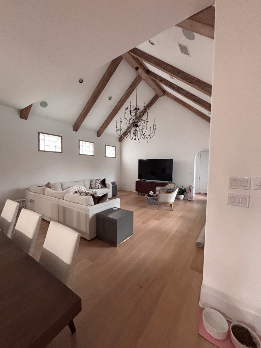 Modern open-plan living room with vaulted ceiling, white sectional sofa, TV, and wooden floors