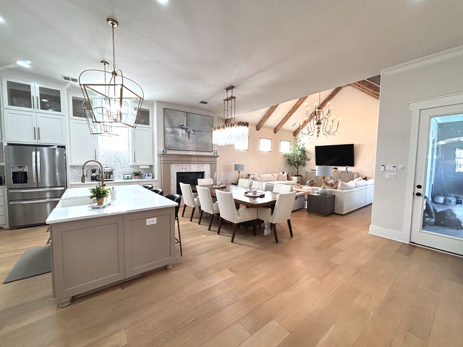 Open-plan kitchen and living room with white cabinets, island, dining table, and vaulted ceiling.