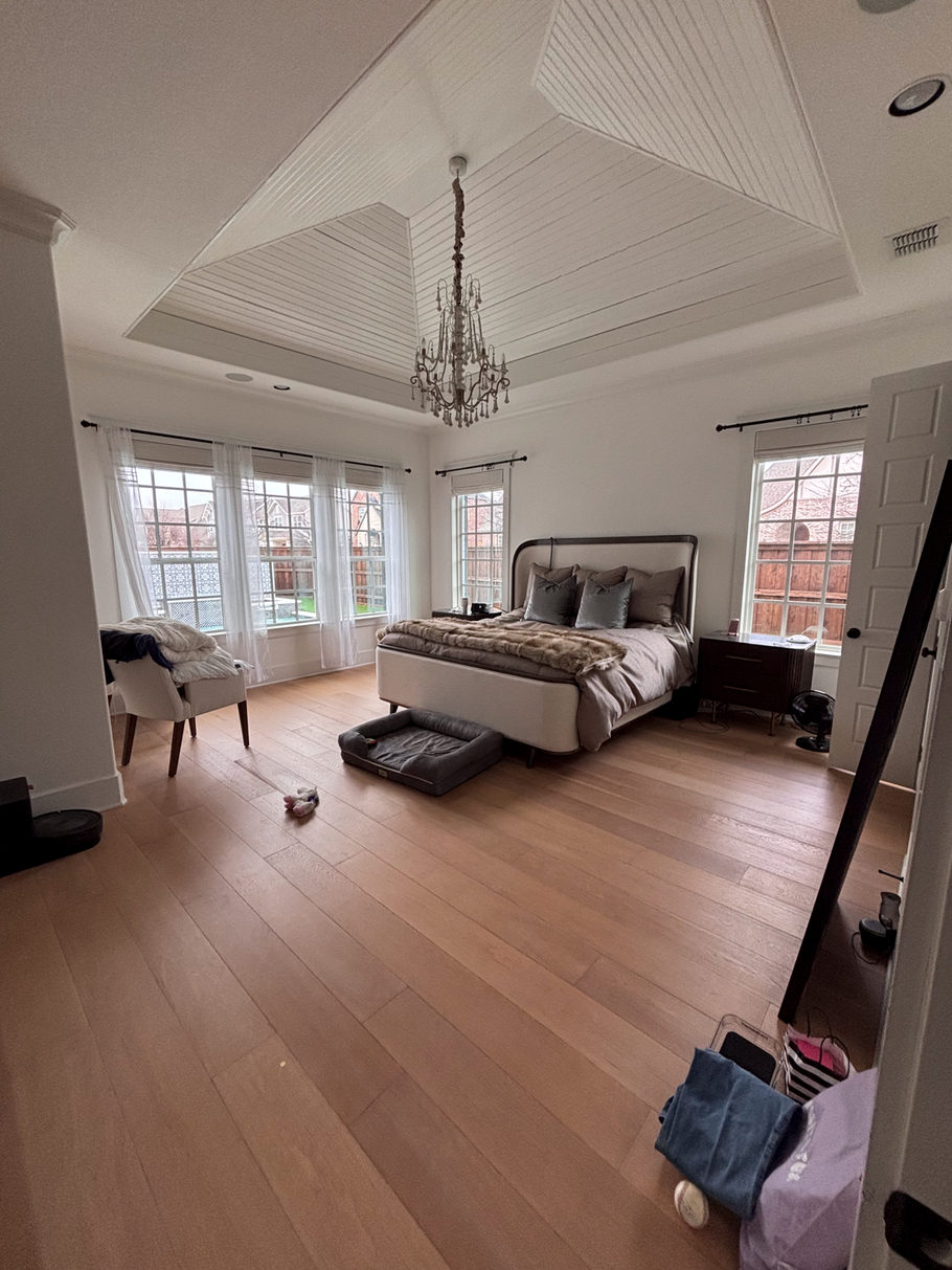 Spacious bedroom with a bed, chandelier, large windows, and light wood floors