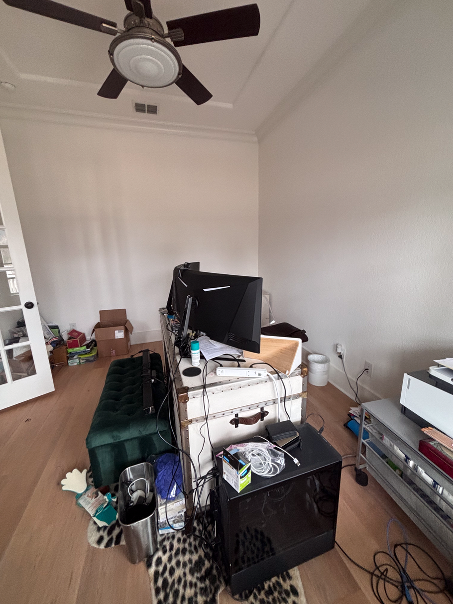 Cluttered room with a TV, fan ceiling, stacked boxes, and household items on the floor