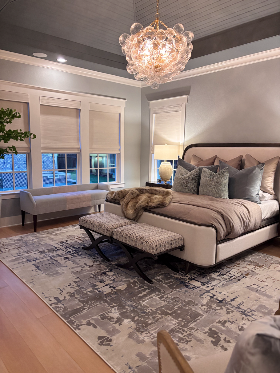 Elegant bedroom with a tufted bed, chandelier, gray walls, and patterned rug by large windows