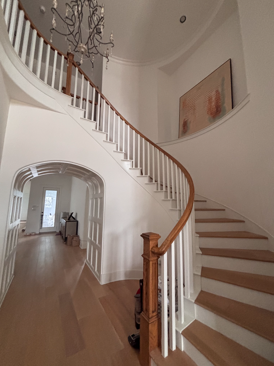 Curved staircase with white railings and wood steps in a bright hallway with a chandelier