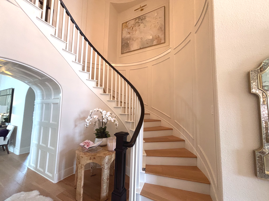 Curved staircase in a bright foyer with beige walls, white railing, and a small table with flowers and decor