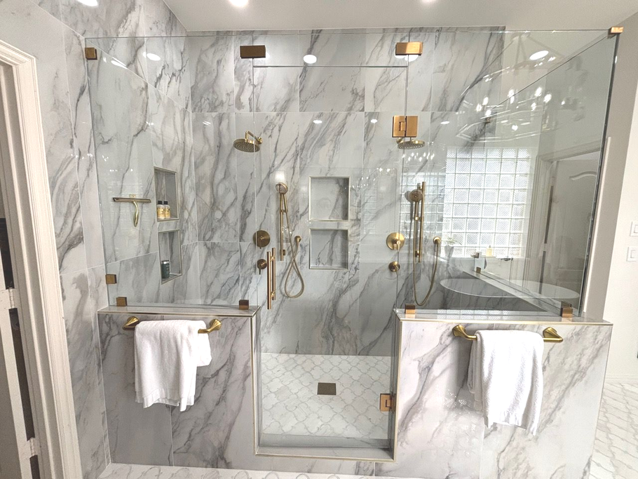 Modern marble bathroom with glass shower, double sinks, and gold fixtures