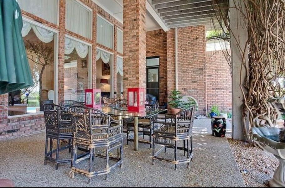 Outdoor patio with wrought-iron chairs, brick walls, and a large tree trunk beside a covered seating area