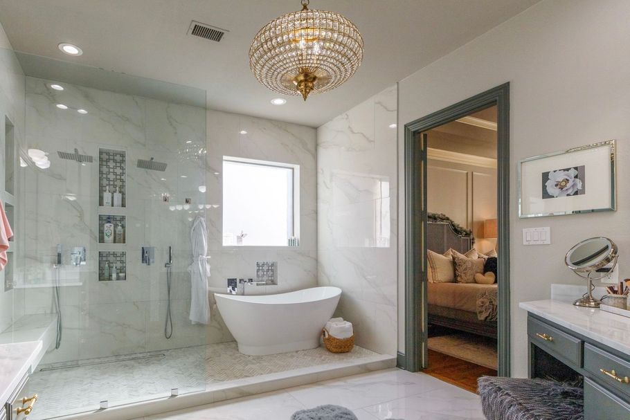 Bright modern bathroom with glass shower, freestanding tub, and crystal chandelier