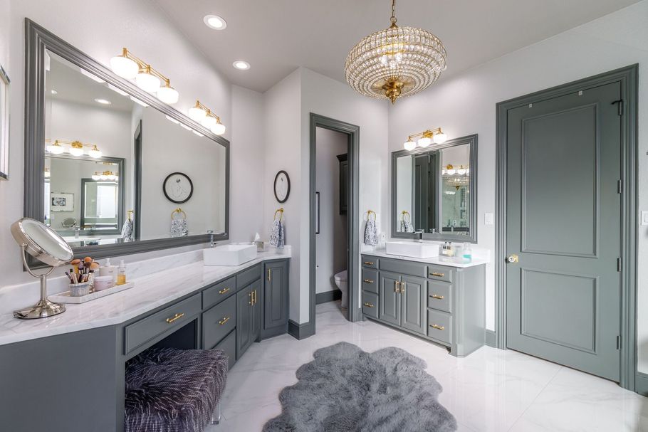 Bright modern bathroom with double vanity, large mirrors, chandelier, and gray doors and cabinets