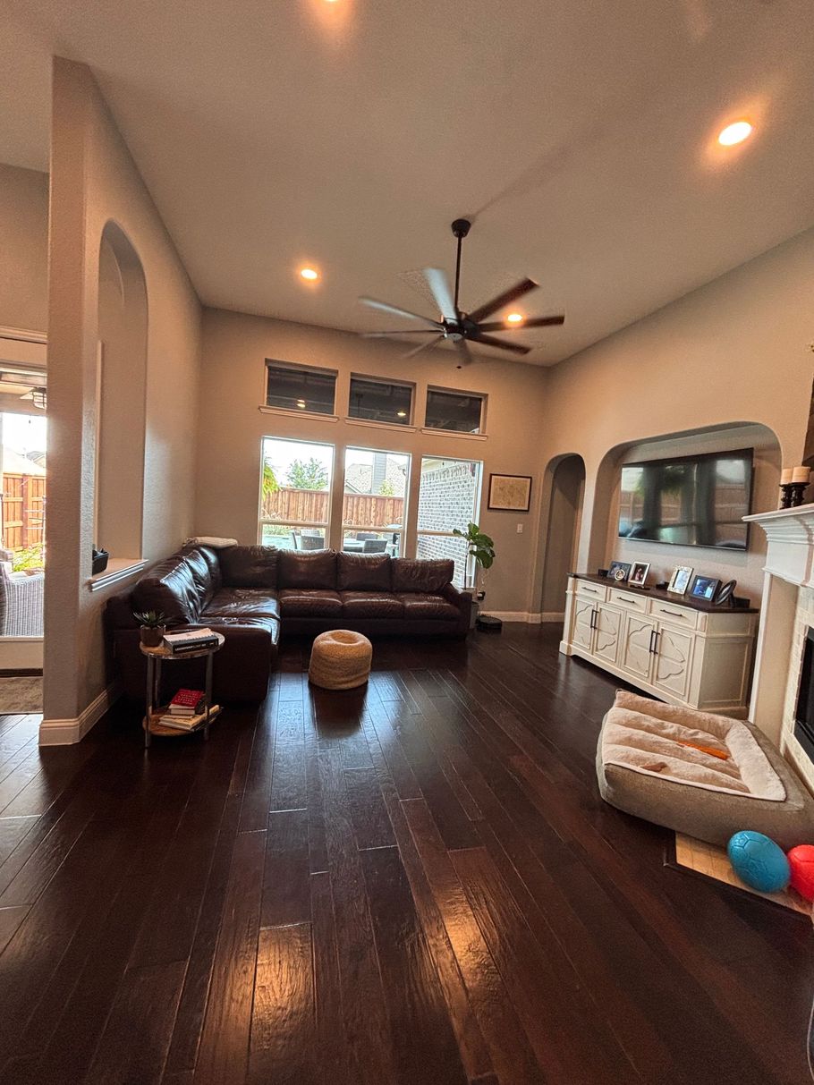 Living room with leather sofa, dark wood floors, ceiling fan, and bright windows; toys on the floor.
