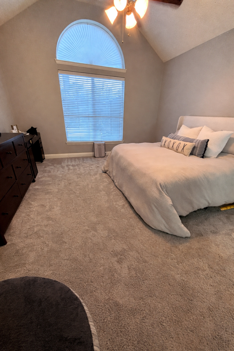 Cozy bedroom with a vaulted ceiling, arched window, beige carpet, and a neatly made bed.