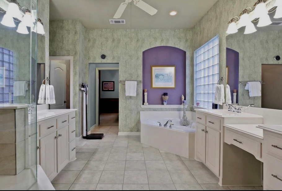 Spacious bathroom with tiled floors, double vanity, large tub, and purple accent wall