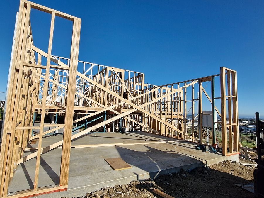 Wooden frame of a house under construction against a blue sky, on a concrete slab foundation.