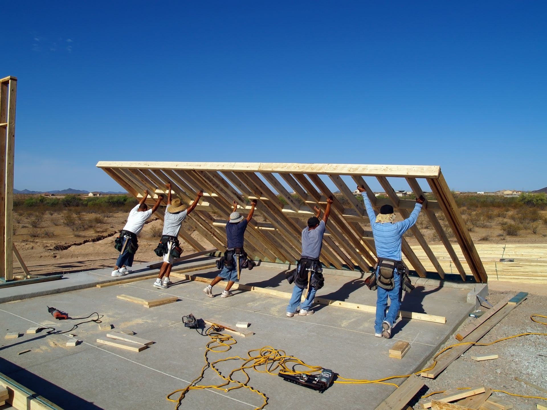Construction workers lifting a wooden wall frame at a building site.