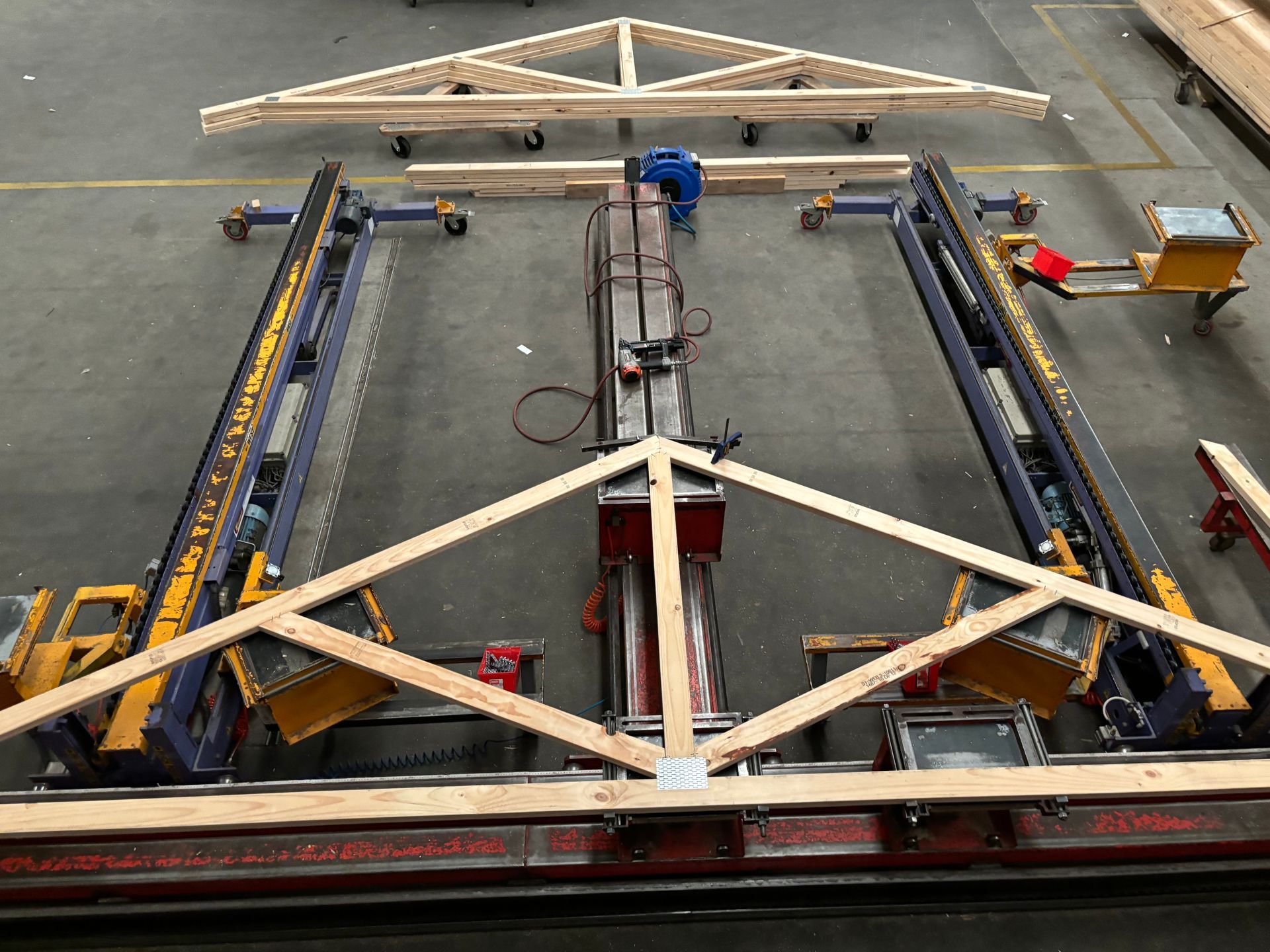 Truss assembly machine constructing a wooden roof truss in a factory setting.