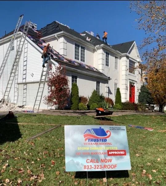 Roofers on a white house, replacing shingles. Sign in foreground for