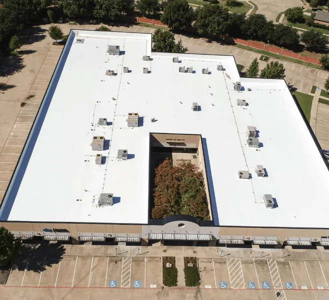 Overhead view of a white commercial building roof with various air vents and a central courtyard of trees.